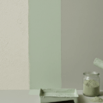 Farbroller trägt pastellgrüne natürliche Wandfarbe auf eine matte Kalkputzwand auf; daneben Malerwanne und offenes Pigmentglas im minimalistischen Studio.