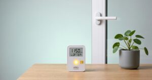 CO2 Ampel auf heller Fläche zeigt gelbes Signal neben Fenstergriff und kleiner Zimmerpflanze