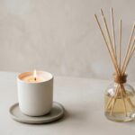 Minimalistisches Stillleben mit brennender Duftkerze und Reed-Diffusor im Studio, weiches Licht, viel Negativraum