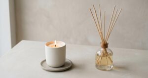 Minimalistisches Stillleben mit brennender Duftkerze und Reed-Diffusor im Studio, weiches Licht, viel Negativraum