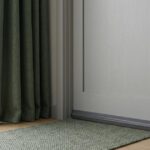 Minimalistisches Stillleben: Türbodendichtung dichtet Schlafzimmer Türspalt ab neben schwerem Vorhang und Teppichläufer