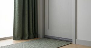 Minimalistisches Stillleben: Türbodendichtung dichtet Schlafzimmer Türspalt ab neben schwerem Vorhang und Teppichläufer