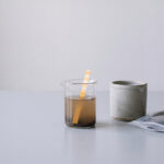 Studio-Stillleben eines pH-Bodentest-Sets mit Erd-Wasser-Becherglas, Probenbeutel und hellgrauem Keramiktopf, symbolisiert sichere Bodenanalyse.
