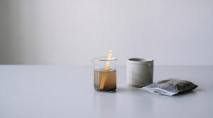 Studio-Stillleben eines pH-Bodentest-Sets mit Erd-Wasser-Becherglas, Probenbeutel und hellgrauem Keramiktopf, symbolisiert sichere Bodenanalyse.